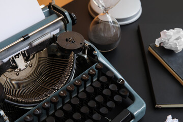 Vintage typewriter with hourglass and notebooks on black table near orange wall