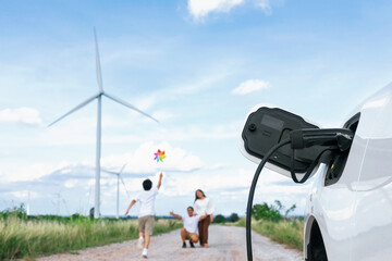 Concept of progressive happy family holding windmill toy and relax at wind farm with electric...