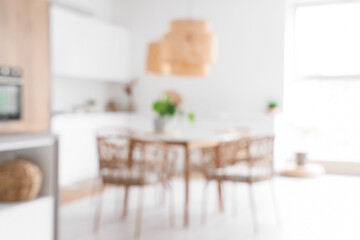 Interior of light kitchen with table, chairs and white counters, blurred view