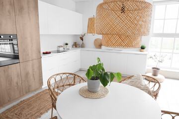 Interior of light kitchen with built-in oven, table, chairs and white counters
