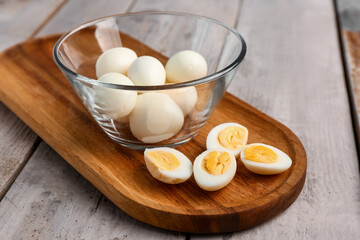 Board with bowl of boiled quail eggs on grey wooden background