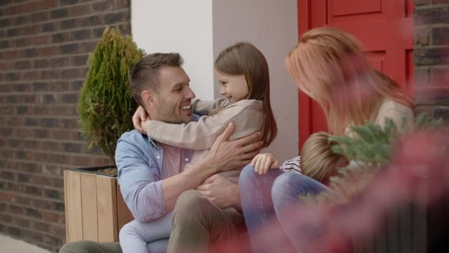 Family with a mother, father, son and daughter sitting outside on steps of a front porch of a brick house