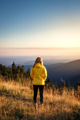 Woman with yellow jacket relax at mountain range during sunset. Hiking in mountains