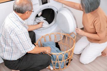 Senior couple working together to complete their household chores at the washing machine in a happy...