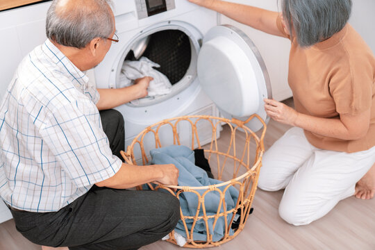 Senior couple working together to complete their household chores at the washing machine in a happy and contented manner. Husband and wife doing the usual tasks in the house.