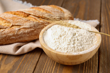 Bowl of wheat flour with fresh bread on brown wooden background