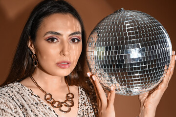 Fashionable beautiful woman in sparkling dress with disco ball on brown background