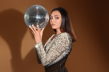Fashionable beautiful woman in sparkling dress with disco ball on orange background