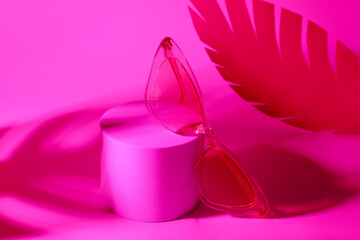 Podium with stylish sunglasses and paper palm leaf on pink background