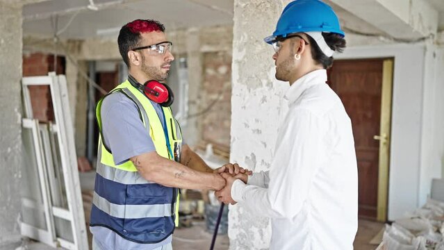 Two men builder and architect shake hands with relaxed expression at construction site