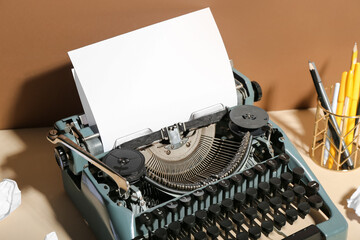 Fototapeta na wymiar Vintage typewriter with stationery holder on beige table near brown wall