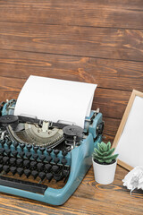 Vintage typewriter with empty frame and houseplant on brown wooden background