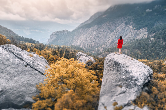 Romantic aerial photo of a girl in a red dress on top of a cliff admiring the view of a mountain gorge