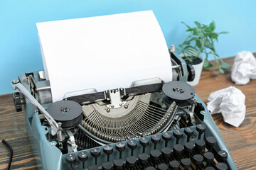 Vintage typewriter with houseplant and crumpled papers on brown wooden table near blue wall