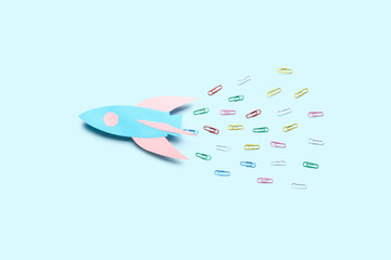Paper rocket with different colorful paper clips on blue background