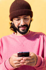 Fototapeta premium portrait of a smiling young man using mobile phone in a yellow background, concept of technology of communication and modern lifestyle