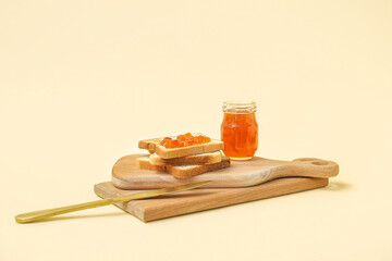 Wooden boards of tasty toasts, apricot jam and knife on pale yellow background