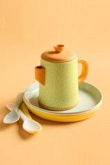 Teapot with plates and spoons for baby on pale orange background