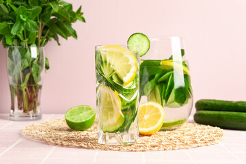 Fototapeta premium Glasses of infused water with cucumber slices on pink tile table