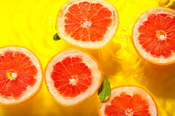 Slices of fresh grapefruit and leaves in water on yellow background