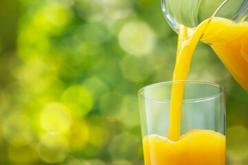 orange juice pouring into glass from jug on green background