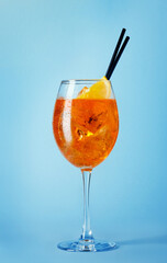glass of aperol spritz cocktail with black straws on blue background