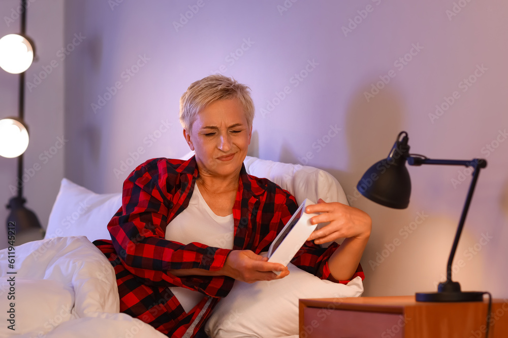 Wall mural Displeased mature woman with clock in bed at night