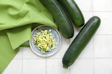 Fresh green zucchini and plate with slices on white tile background