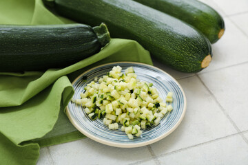Fresh green zucchini and plate with slices on white tile background