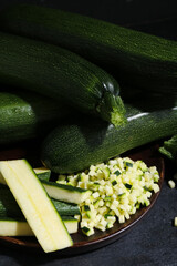 Many fresh zucchini and tray with slices on black table