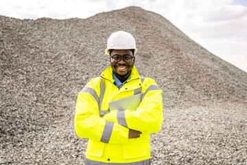 Supplier in safety helmet standing in front of large pile of rock selling construction material.