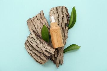 Bottle of essential oil, tree bark and plant leaves on color background