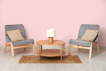 Armchairs with wooden coffee table, lamp and floor mat near pink wall