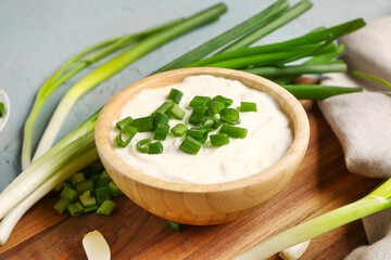 Obraz na płótnie Canvas Board and bowl of tasty sour cream with sliced green onion on blue background