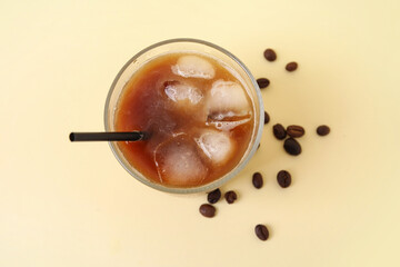 Glass of ice coffee with straw and beans on yellow background