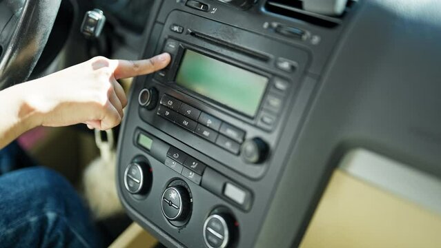 Young Beautiful Hispanic Woman Sitting On Car Turning On Radio At Street