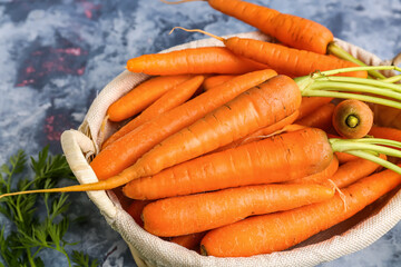 Wicker basket with fresh carrots on blue background