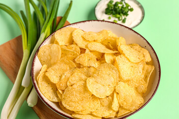 Bowl of tasty sour cream with sliced scallion and potato chips on green background