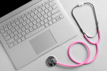 Stethoscope and laptop on light  background, top view