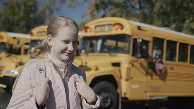 Portrait of a schoolgirl in front of a row of school buses