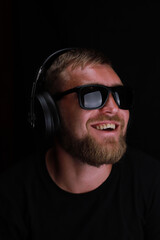 Young bearded man listening to music with headphones on a black background