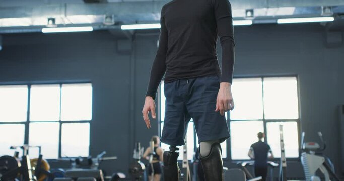 young ambitious disabled man standing confidently on prothesis legs at gym Slow motion cross fit