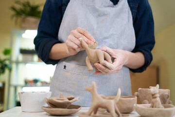 woman sculpts a figurine of a dsnosaur from clay by hands, closeup in artistic studio