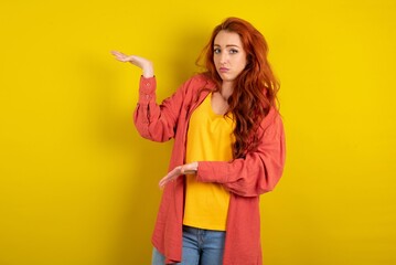 young beautiful red haired woman pointing aside with both hands showing something strange and...