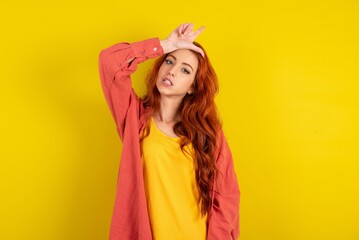 young beautiful red haired woman making fun of people with fingers on forehead doing loser gesture mocking and insulting.