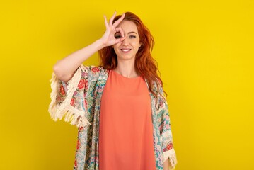 young beautiful red haired woman doing ok gesture with hand smiling, eye looking through fingers with happy face.