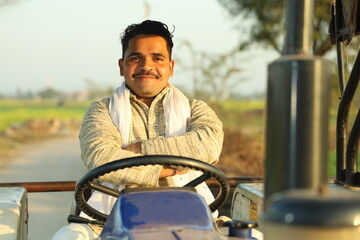 Happy Indian villager farmer sitting on the tractor enjoying the village life.