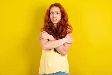 Desperate young beautiful red haired woman wearing yellow blouse over yellow studio background...