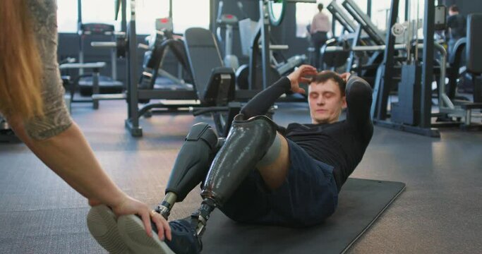 motivated strong man with prosthesis doing abdominal crunches, disabled man working out at gym. sportsman doing ABS, focus on artifical legs, strength training endurance, willpower