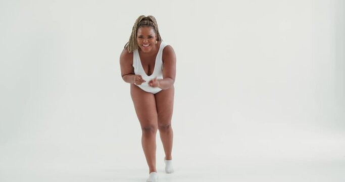 laughing fit sporty plump African woman in white swimsuit having fun in studio, Slow motion. Afro happy overweight girl pointing to camera, plump dancer having rest break after workout. hobby